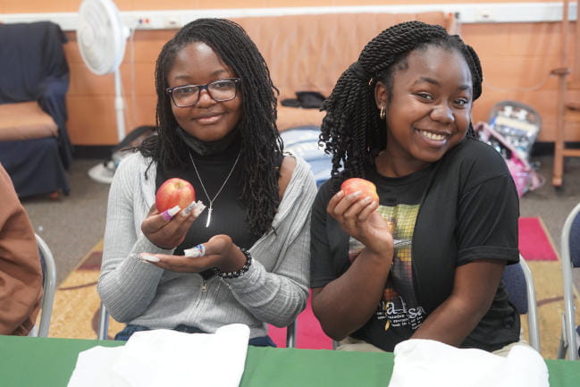Two school students pose and hold up apples.